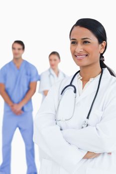 Smiling doctor with arms folded and colleagues behind her against a white background