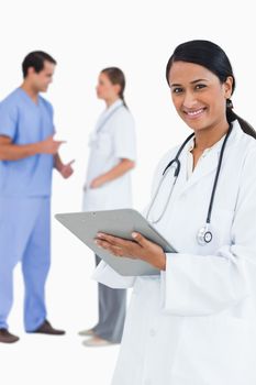 Smiling doctor with clipboard and staff members behind her against a white background