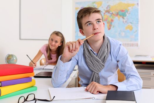 Photo of a handsome young male student thinking in class with a female student in the background.
