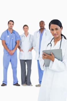 Female doctor with clipboard and colleagues behind her against a white background