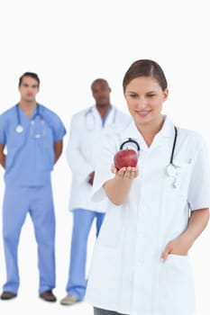 Doctor looking at apple with colleagues behind her against a white background