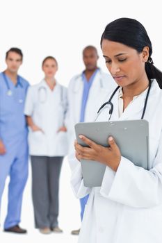 Female doctor reading notes with staff members behind her against a white background