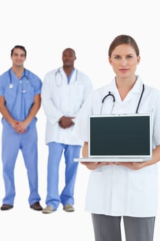 Female doctor showing laptop with colleagues behind her against a white background
