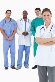 Smiling doctor with folded arms and colleagues behind her against a white background