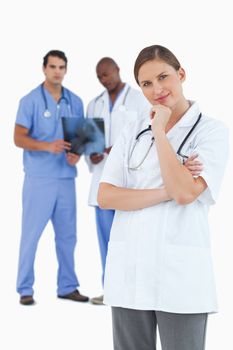 Doctor in thinkers pose with colleagues behind her against a white background