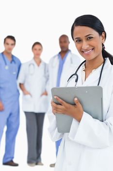 Smiling female doctor with clipboard and staff behind her against a white background