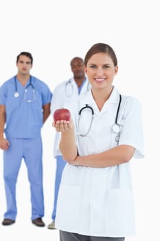 Smiling doctor with apple and colleagues behind her against a white background