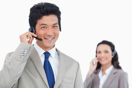 Smiling call center agent with colleague behind him against a white background
