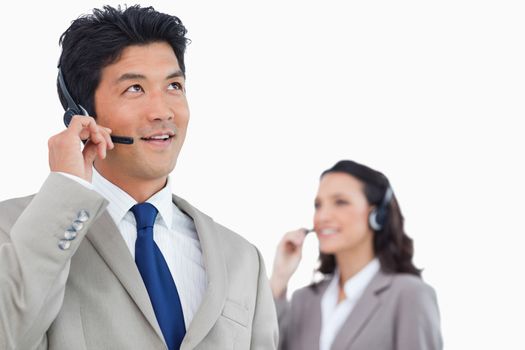 Call center agent with headset and colleague behind him against a white background
