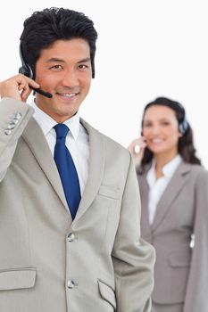 Smiling customer support employee with colleague behind him against a white background