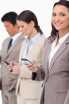 Smiling businesswoman with cellphone next to colleagues against a white background