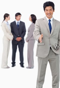 Businessman with team behind him offering hand against a white background