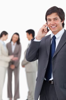 Smiling salesman on cellphone with team behind him against a white background