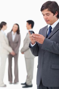 Salesman reading text message on cellphone with team behind him against a white background