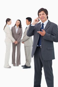 Salesman talking on cellphone with team behind him against a white background