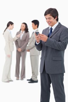 Smiling salesman holding mobile phone with team behind him against a white background