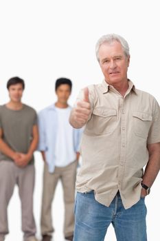 Senior man giving thumb up with young people behind him against a white background