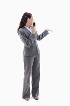Businesswoman announcer speaking in a microphone and looking behind against white background