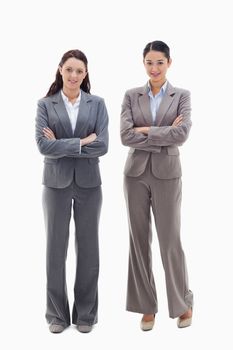 Two businesswomen smiling and crossing their arms against white background