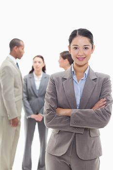 Businesswoman smiling and crossing her arms with co-workers talking in the background