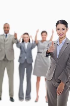 Close-up of a businesswoman approving with hand gesture with enthusiastic co-workers raising their arms in the background