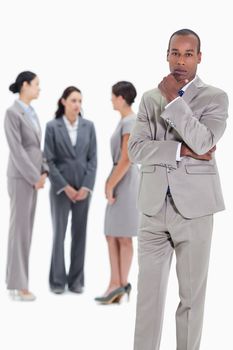 Serious businessman with a hand on his chin and three female co-workers talking seriously in the background