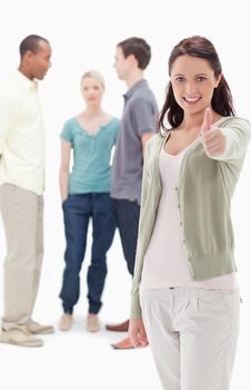 Girl smiling and giving the thumbs-up with friends chatting in background