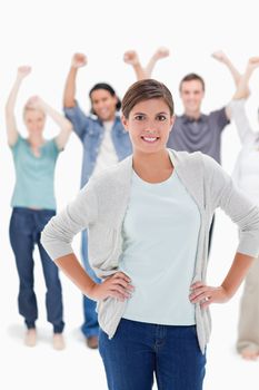 Close-up of a woman with her hands on her hips with people behind raising their arms against white background