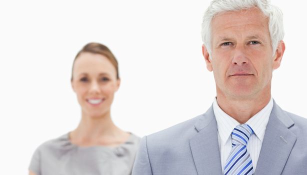 Close-up of a serious white hair businessman with a woman smiling behind him against white background
