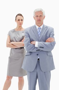 Serious white hair businessman with a woman behind him crossing their arms against white background