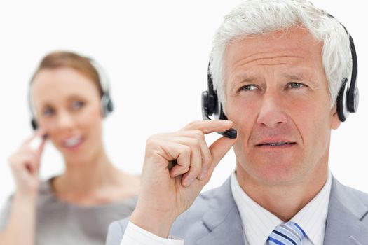 Close-up of a white hair man with a woman talking in background while wearing a headset against white background