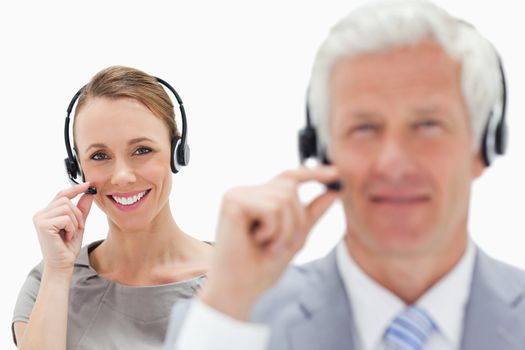 Close-up of a smiling woman talking in background with a white hair man while wearing a headset against white background