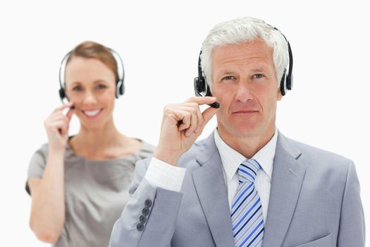 Close-up of a white hair man with a smiling woman in background wearing a headset against white background