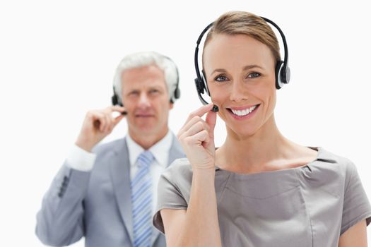 Close-up of a smiling woman wearing a headset with a white hair businessman in background