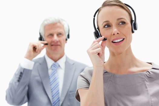 Close-up of a woman talking and wearing a headset with a white hair businessman in the background