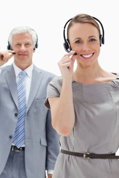 Close-up of a woman smiling and wearing a headset with a white hair businessman in the background