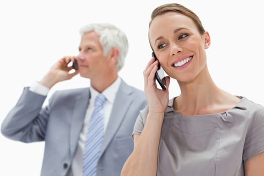 Close-up of a smiling woman making a call with a white hair businessman in background against white background