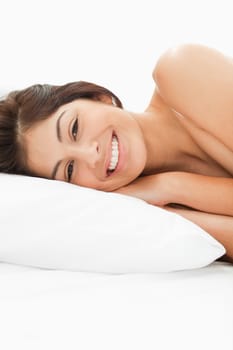 A woman lying on the bed with her head on the pillow she is awake and smiling, with her hands on the pillow.