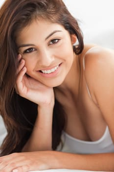 A close up shot of a smiling woman who is looking forward with a hand upon her cheek. 