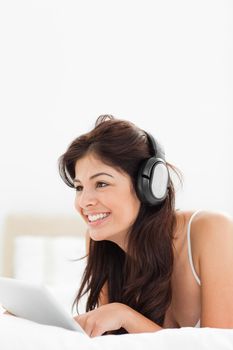 A woman using enjoying the use of her tablet and headphones while lying on the bed.