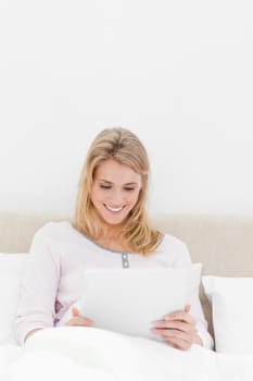 A centered shot of a woman in watching a tablet pc while sitting in bed and smiling.