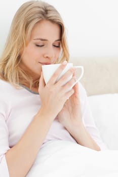 A close up shot of a woman holding a cup up to her face, with her eyes closed. Smelling the contents of the cup.