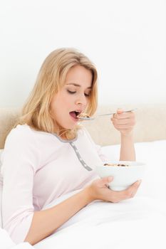 A woman sitting in bed, with a bowl in hand, and about to eat a spoon of cereal.