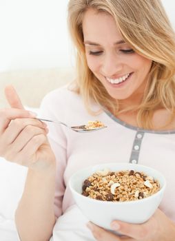 A close up shot of a woman holding a bowl of cereal and a raised spoon of cereal near to her mouth.