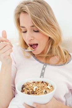 A close up shot of a woman holding a bowl of cereal and a raised spoon of cereal she is about to eat.