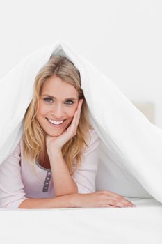 A close up shot of a woman smiling as she lies under a quilt with her hand supporting her head.