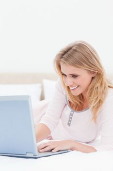 A close up shot of a smiling woman lying on the bed using a laptop