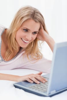 A close up shot of a woman using her laptop and smiling while lying on the bed.