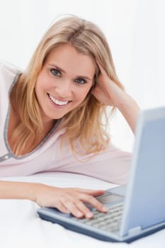 A close up shot of a woman lying on her bed, with her laptop beside her.