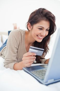 A close up shot of a woman smiling with a credit card in hand and laptop in front of her.